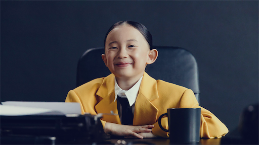 Mädchen im gelben Anzug sitzt am Schreibtisch und lächelt selbstbewusst